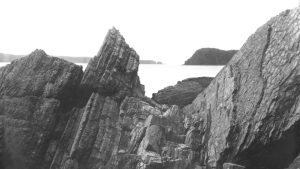 Rocky shoreline with layered rock framing open water and Cape Split and Cape Sharp on the horizon